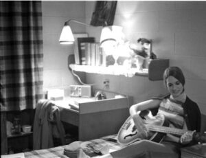 A woman playing guitar in a Threlkeld dorm room in 1969