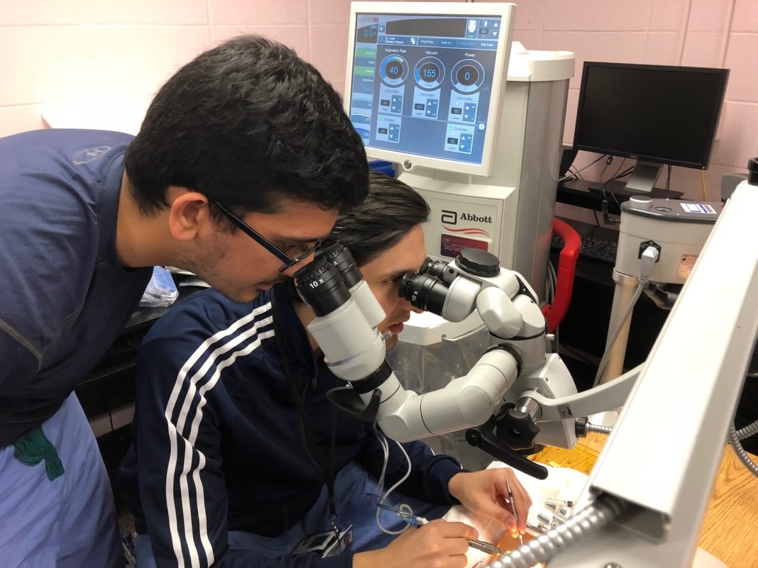 Ophthalmology residents Sidharth Puri, M.D., standing, and Mohammad Ali Sadiq M.D., training in cataract eye surgery using artificial eyes in a ‘wet lab’ at the University of Louisville
