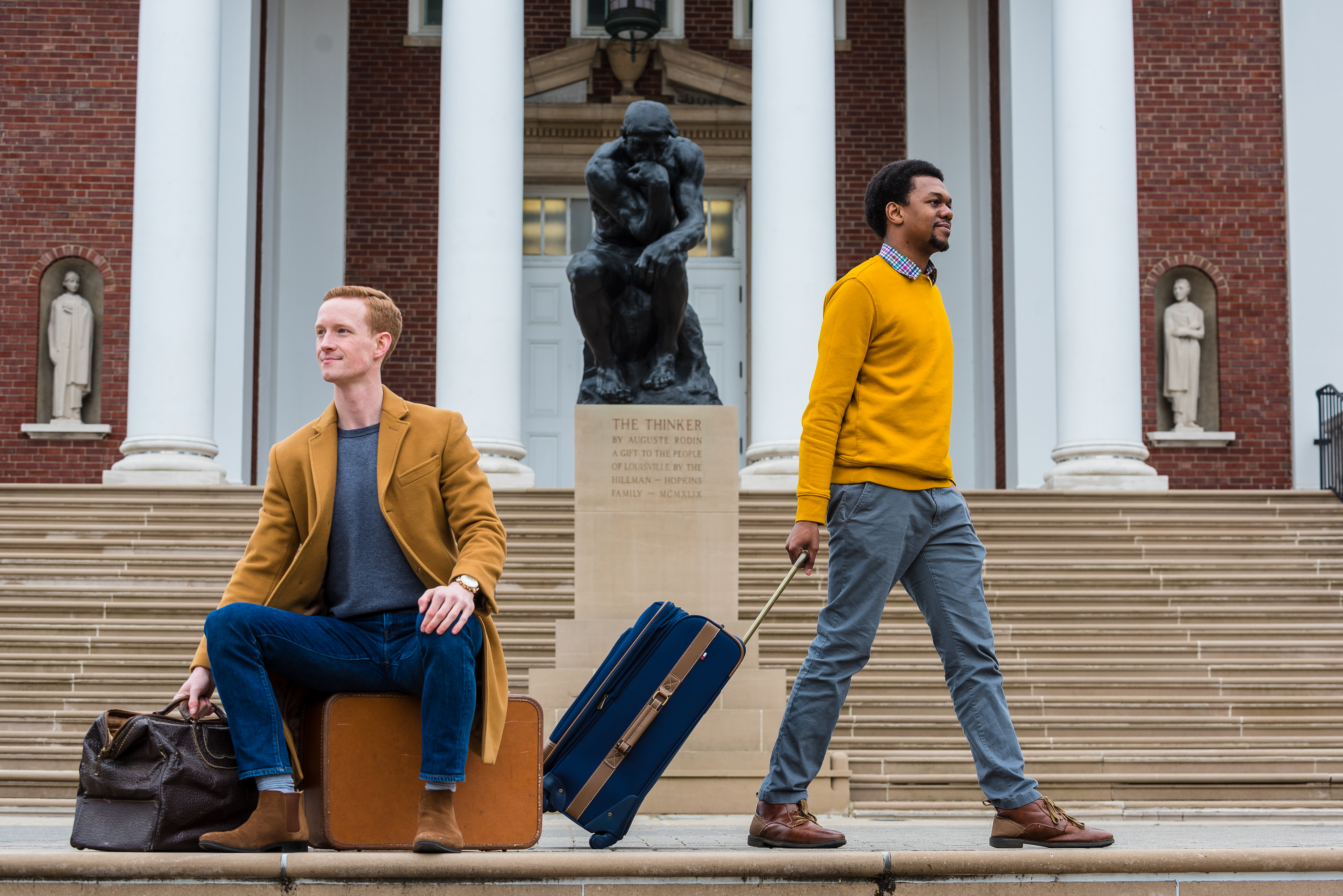 Chris Bird and Kavonte Jones with luggage in front of the Thinker statue on UofL's campus