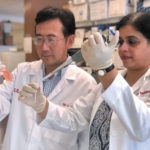 Professors Chi Li and Kavitha Yaddanapudi, co-inventors of a cancer vaccine, in white coats testing chemicals in a lab.