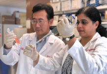 Professors Chi Li and Kavitha Yaddanapudi, co-inventors of a cancer vaccine, in white coats testing chemicals in a lab.