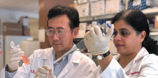Professors Chi Li and Kavitha Yaddanapudi, co-inventors of a cancer vaccine, in white coats testing chemicals in a lab.