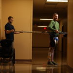 Jeff Marquis uses horizontal poles to help him balance during therapy in the hallway of Frazier Rehab Institute. He is assisted by Curtis Standafer.