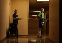 Jeff Marquis uses horizontal poles to help him balance during therapy in the hallway of Frazier Rehab Institute. He is assisted by Curtis Standafer.