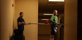 Jeff Marquis uses horizontal poles to help him balance during therapy in the hallway of Frazier Rehab Institute. He is assisted by Curtis Standafer.