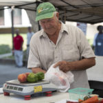 A vendor weighs produce at the Gray Street Farmers Market.