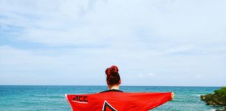 Cheyenne Hill holds a UofL flag overlooking a beach in Trinidad and Tobago.