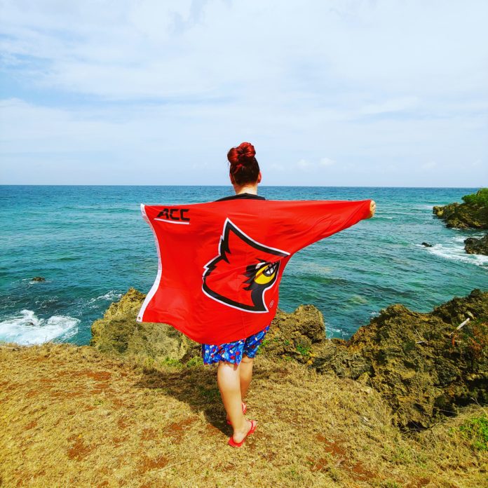 IMG_20200320_180108_592 Cheyenne Hill holds a UofL flag overlooking a beach in Trinidad and Tobago.