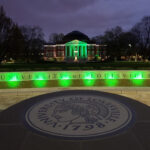 Picture of the university oval entrance and Grawemeyer Hall lit up at night in green to honor COVID-19 victims.