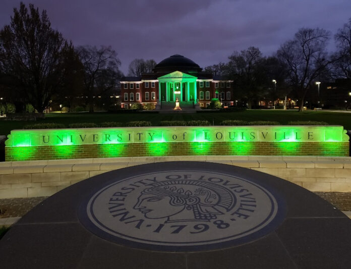 Picture of the university oval entrance and Grawemeyer Hall lit up at night in green to honor COVID-19 victims.