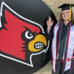 Christel Blocker stands in front of a Cardinal head in her cap and gown.