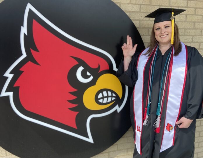 Christel Blocker stands in front of a Cardinal head in her cap and gown.