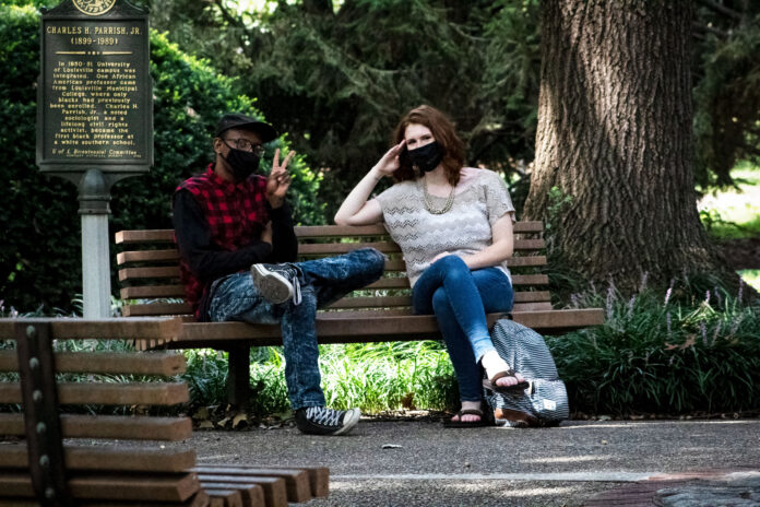 Masked students talk on a bench