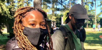 Female student, Kenyetta Johnson, holding a dragonfly in her hand while wearing a black mask on her face.