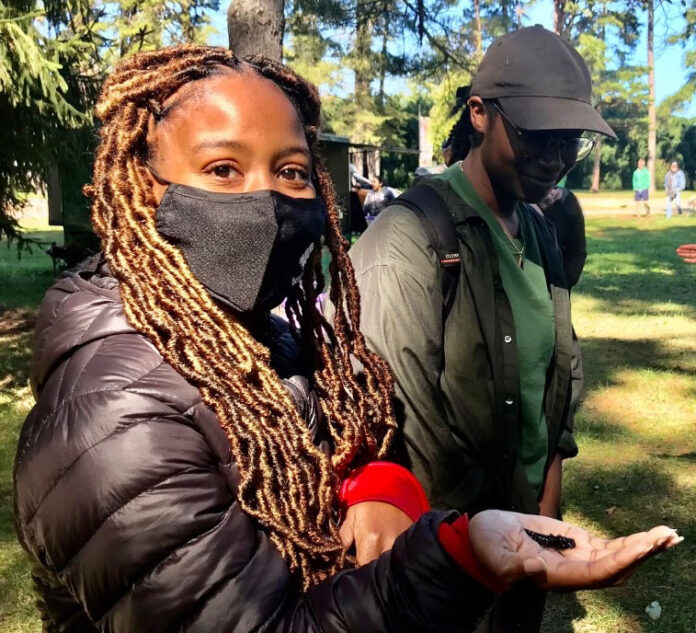 30F14C3C-DD95-4701-A4BA-FD30D028F27B Female student, Kenyetta Johnson, holding a dragonfly in her hand while wearing a black mask on her face.