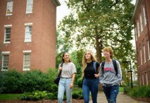 Three students wearing UofL shirts and carrying backpacks walk on a sidewalk on UofL's campus