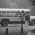 black and white image of a boy jumping in the pouring rain with a bus in the background