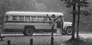 black and white image of a boy jumping in the pouring rain with a bus in the background