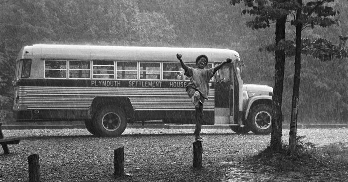 black and white image of a boy jumping in the pouring rain with a bus in the background