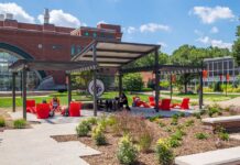 students at tables, chairs, underneath a pergola on a lawn
