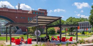 students at tables, chairs, underneath a pergola on a lawn