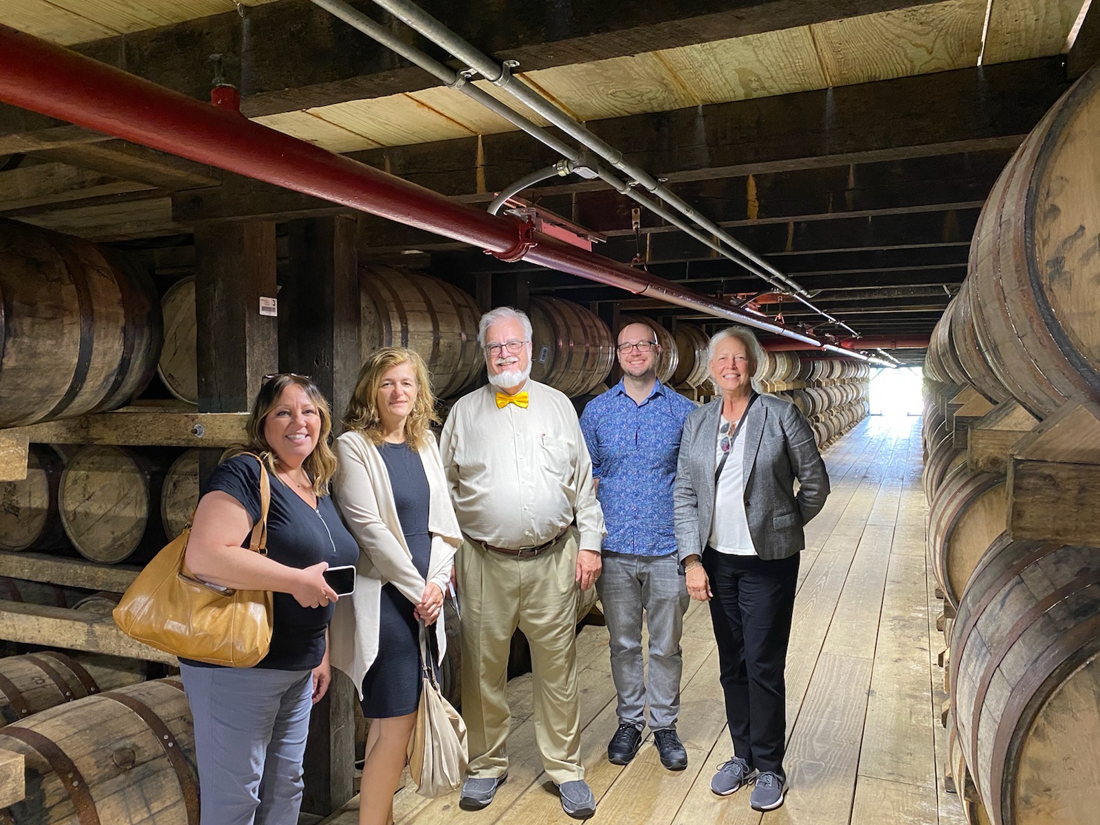 Manuela Perri, Julijana Curcic, Bob Hausladen, Alex Bryant and Virginia Denny of the UofL College of Business executive education program in a barrel house at Jim Beam Distillery.