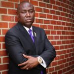 Benjamin Crump with arms folded standing against a red brick wall