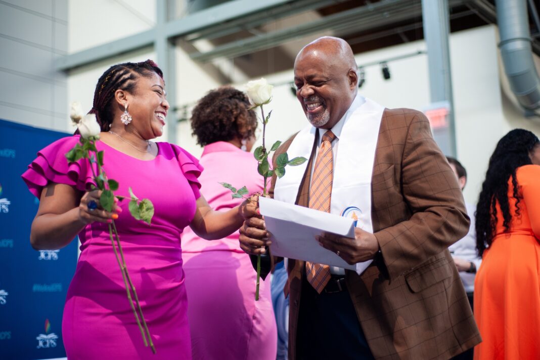 Woman hands a flower to a man holding an envelope with graduation certificate.
