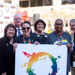 Group of health care leaders posing with LGBT Center poster in pride apparel.