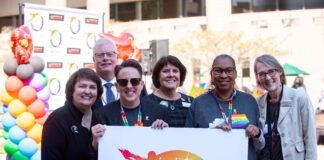 Group of health care leaders posing with LGBT Center poster in pride apparel.