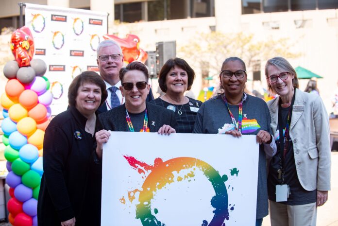 Group of health care leaders posing with LGBT Center poster in pride apparel.