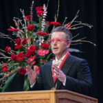 Rev. Charles Halton speaks at a podium with large roses behind him.
