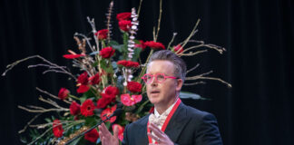 Rev. Charles Halton speaks at a podium with large roses behind him.