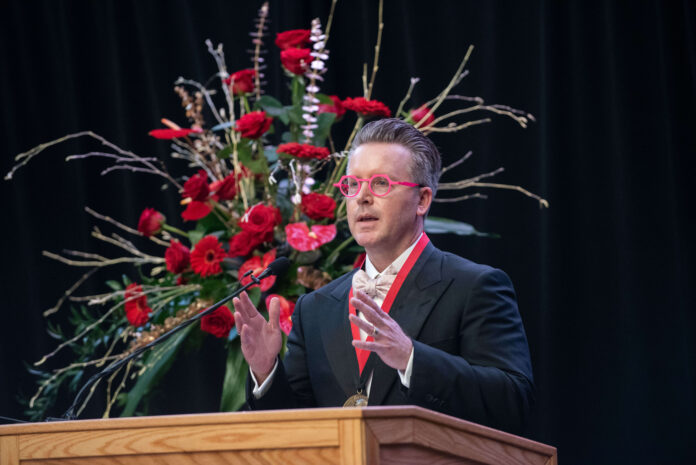 Rev. Charles Halton speaks at a podium with large roses behind him.