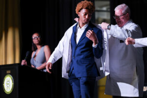 Jeffrey Bumpous, interim dean of the UofL School of Medicine, right, placed a white coat on the shoulders of a Central High School junior participating in the Pre-Medical Magnet Program. UofL Health photo.
