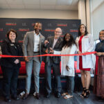 Several people cut a red ribbon with a large pair of scissors.