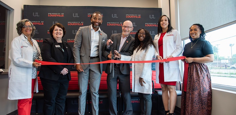 Several people cut a red ribbon with large scissors.