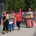 Students and volunteers move boxes and rolly carts into a residence hall on UofL's campus.