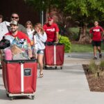 Students and families pushing red carts with their belongings.