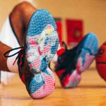 UofL Athletics Louie shoes close up with an image of Louie dunking a basketball. Basketball player wearing the shoes is sitting in the background with a basketball propped against their feet.