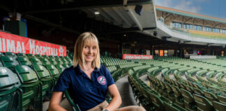 a woman in professional clothing sits at a baseball stadium
