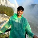 Man in rain poncho in front of a large waterfall with a rainbow behind him