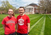 Two people wearing UofL tshirts smile in a grassy lawn.