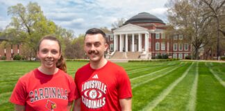 Two people wearing UofL tshirts smile in a grassy lawn.