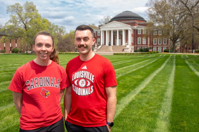 Two people wearing UofL tshirts smile in a grassy lawn.