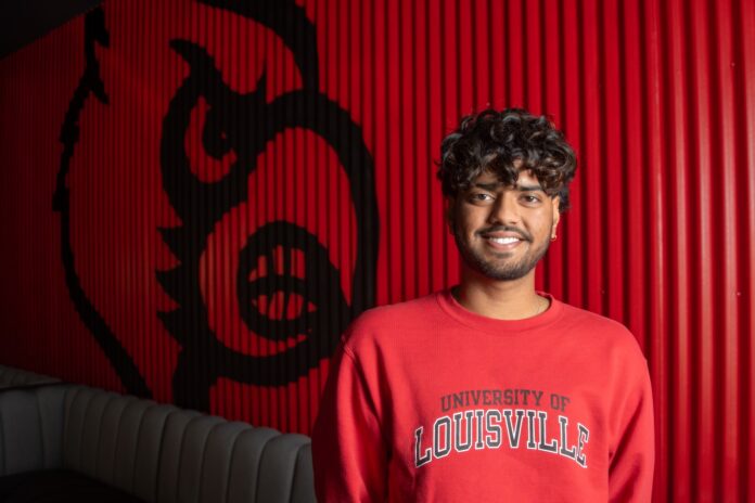 KamalA_edited Man in red UofL shirt with Cardinal on wall behind him.