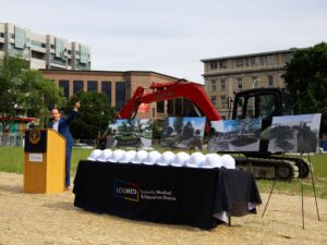 Man at podium with construction equipment and table with hardhats
