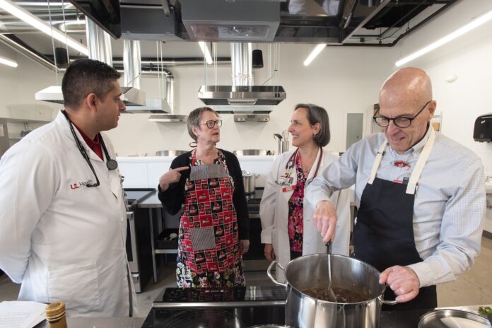 Trager Kitchen_7364 Group talking MED Four adults talking in a commercial-style kitchen