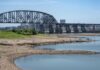 Banks of a river with a railroad bridge and Louisville skyline in the background