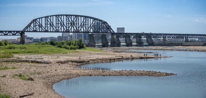 Banks of a river with a railroad bridge and Louisville skyline in the background